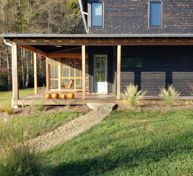 Scandinavian farmhouse renovation featuring a screened in wrap around porch and burnt wood siding